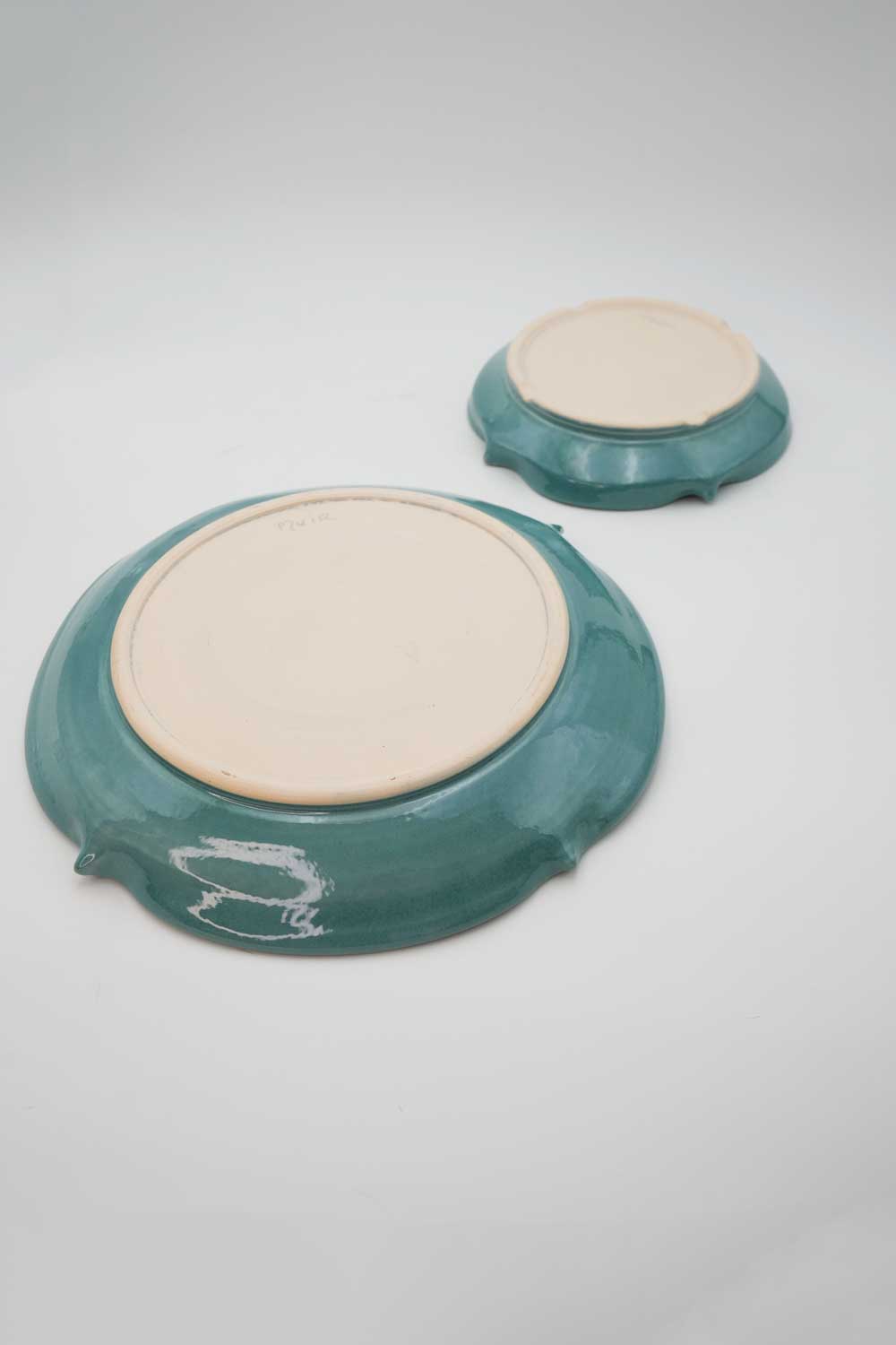 The underside of two handmade ceramic turquoise bowls showing a cream color clay body.