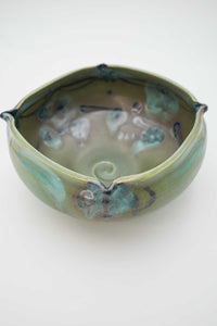 A medium size, hand thrown ceramic bowl with fluted edges.  Dominate color is sage green.