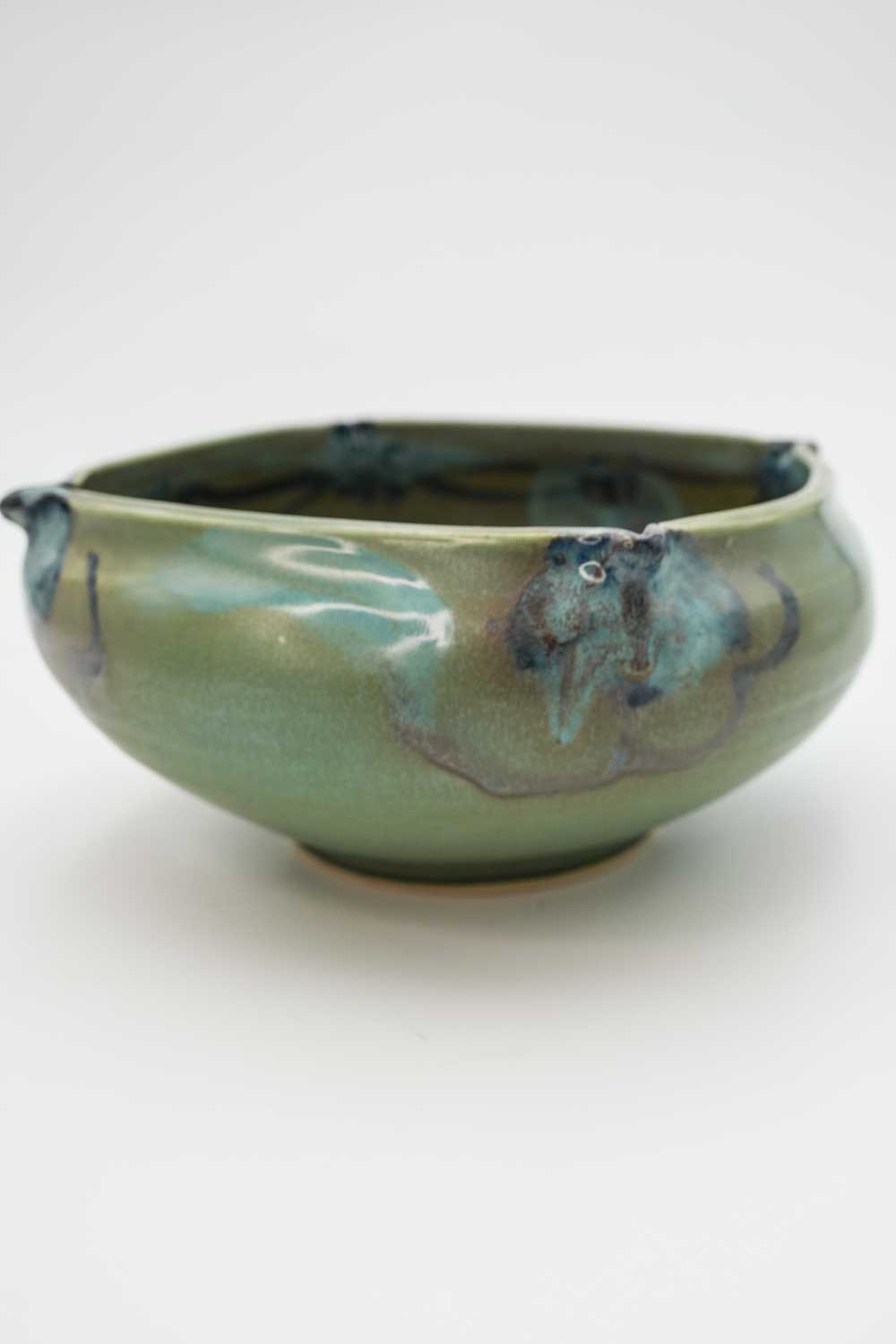 A medium size, hand thrown ceramic bowl with fluted edges.  Dominate color is sage green.  Painted with abstract blue flowers.